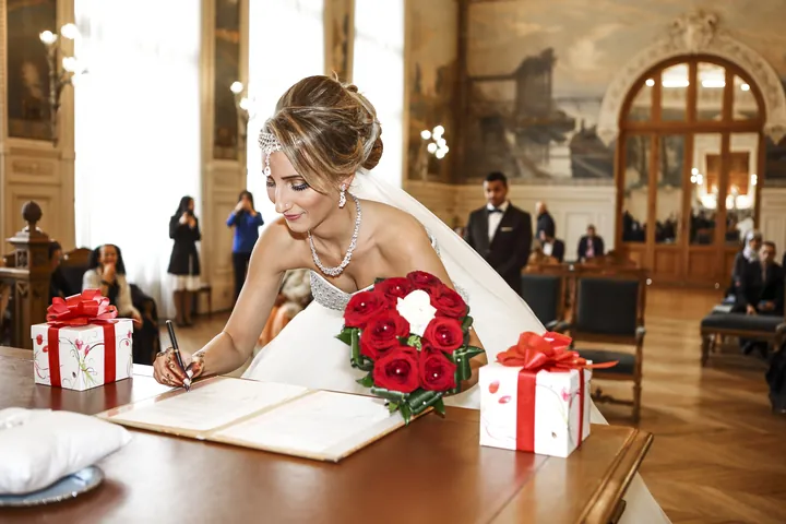 Mariée qui signe le registre à la mairie, bouquet de roses rouges sur la table